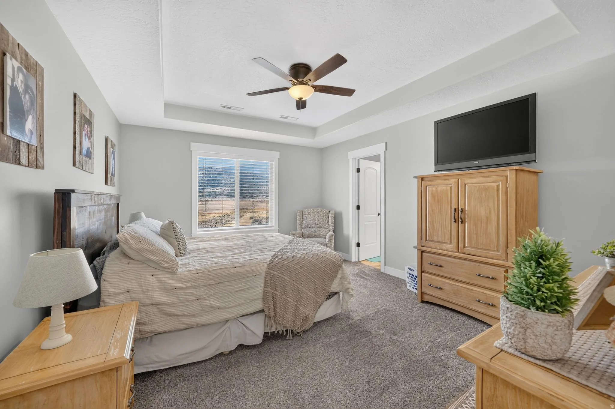 Tray ceiling with a ceiling fan light fixture, light gray walls, and large window with blinds