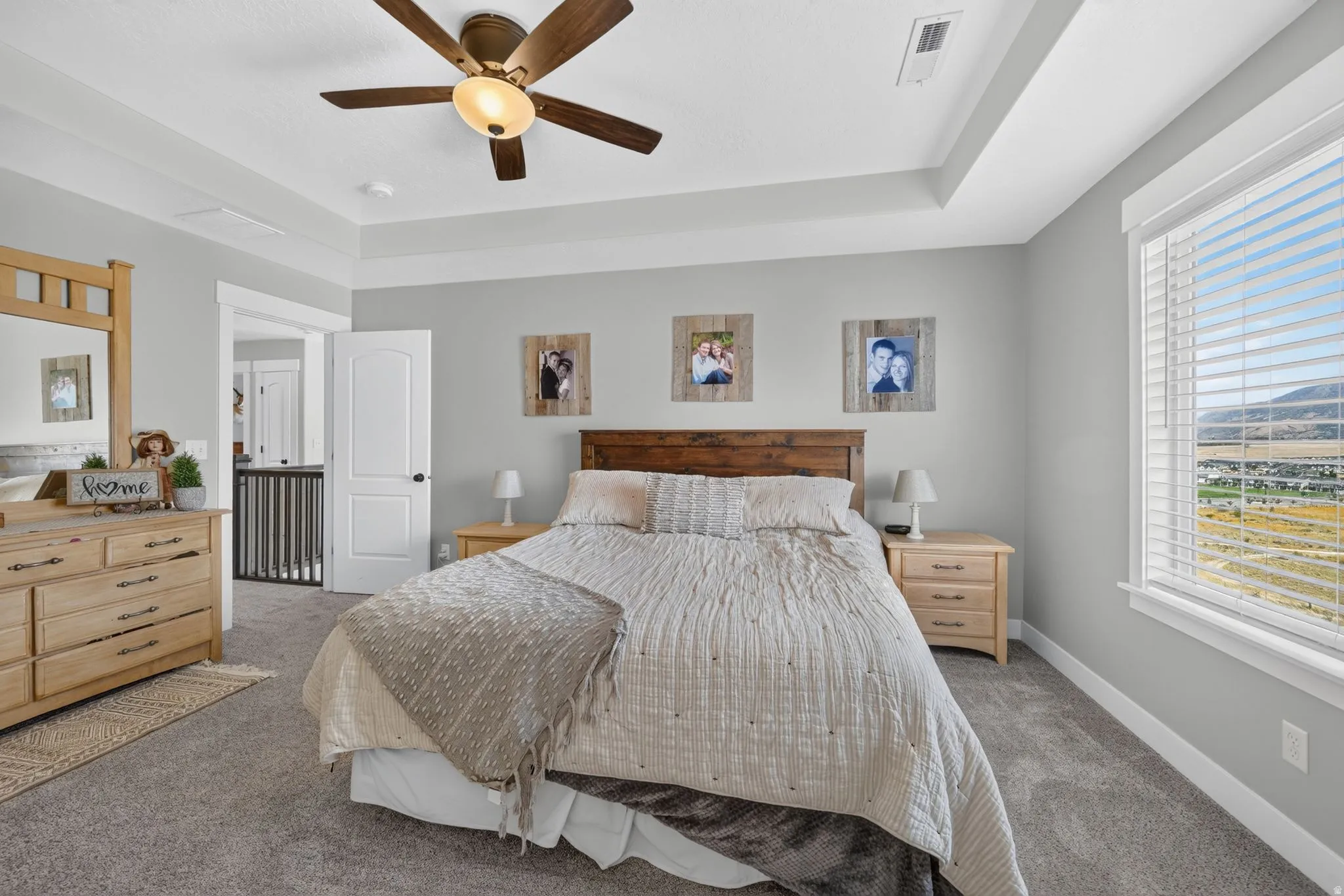 Tray ceiling with a ceiling fan, light gray wall paint, and a large window with blinds