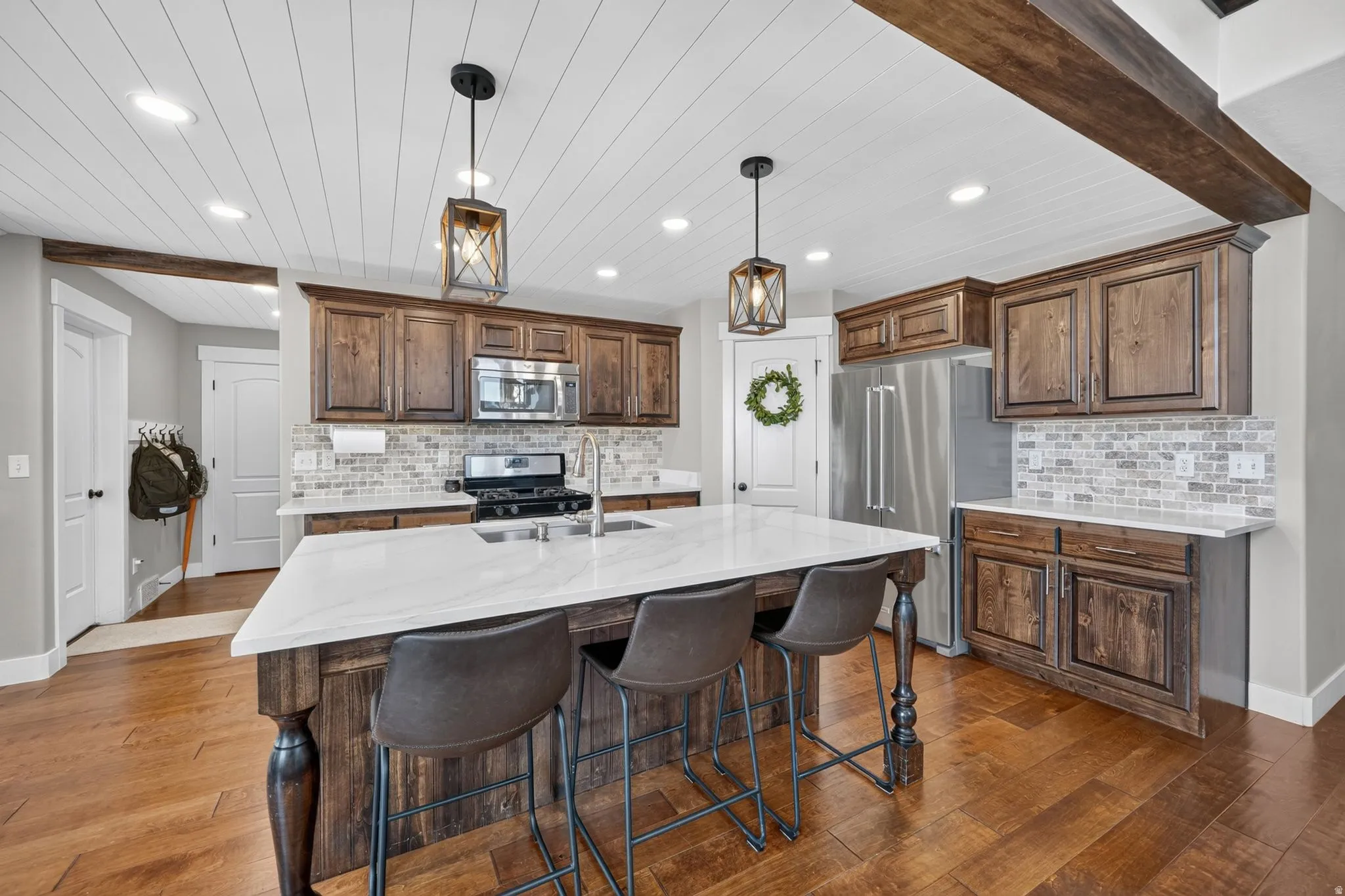 Kitchen featuring wood-finish flooring, wood cabinetry, stainless steel appliances, a center island with a white countertop, and a tile backsplash