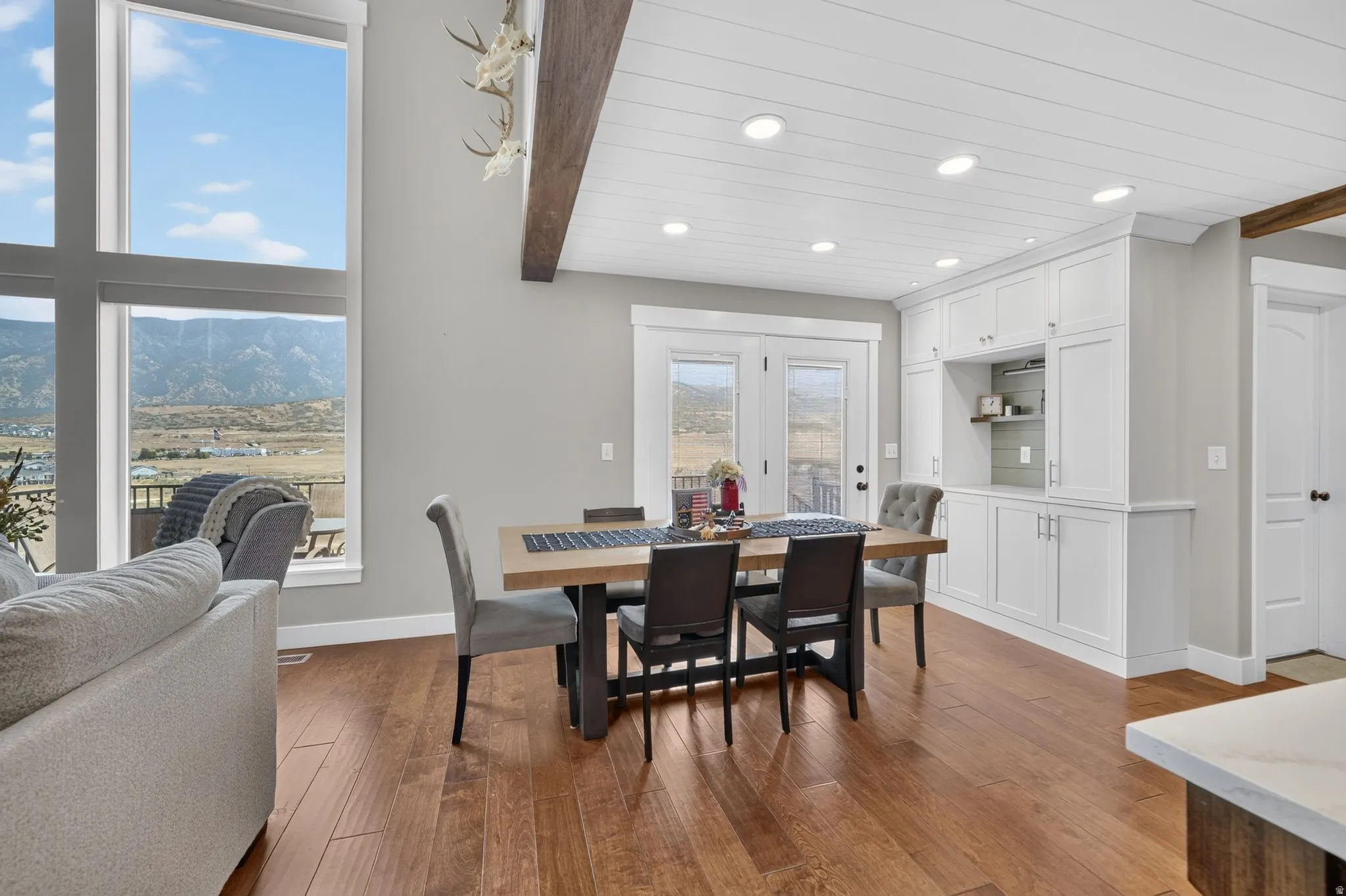 Hardwood flooring throughout, tall windows, white built-in cabinetry, exposed wood beam, and French doors