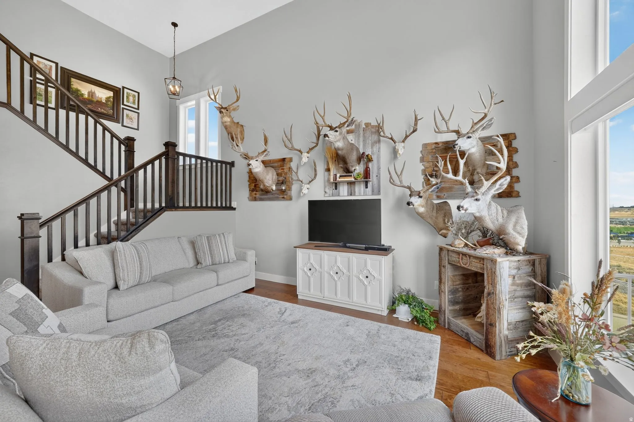 Two-story living area with hardwood flooring, large windows, and a staircase featuring dark wood railing
