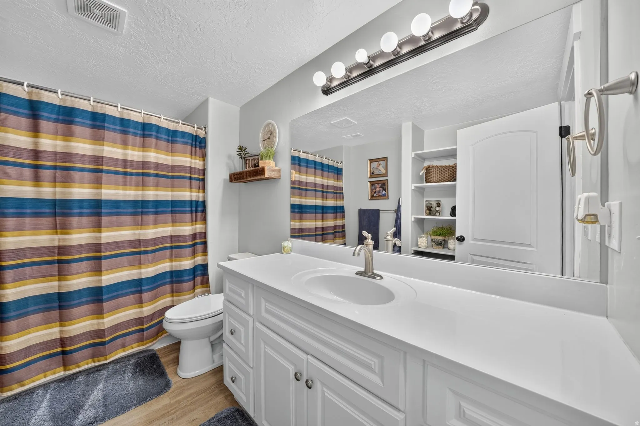 White vanity with dual sinks, brushed nickel fixtures, a large mirror, and overhead vanity lighting