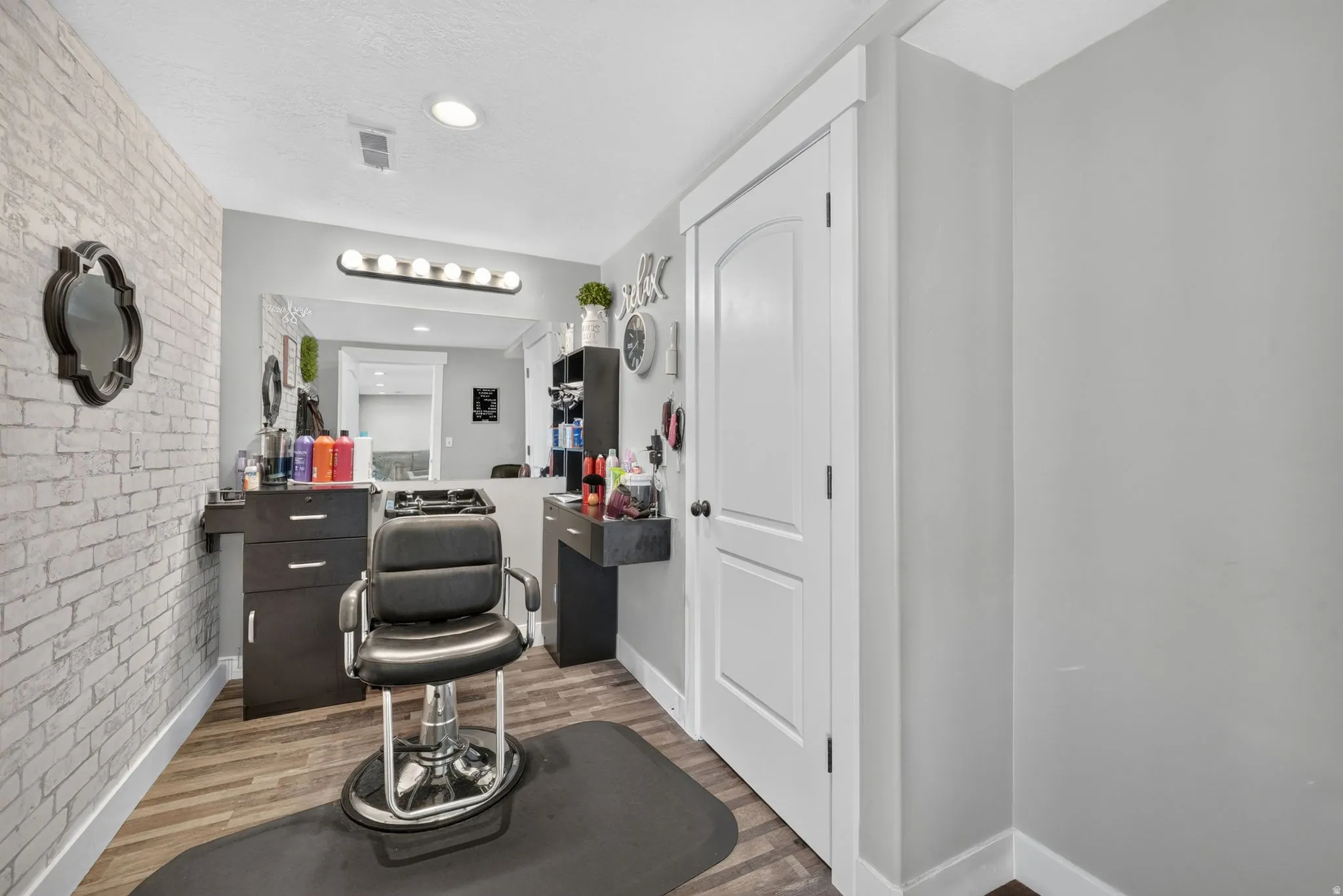Wood-finish flooring with a light-toned brick accent wall, recessed lighting, and a solid white door with dark hardware