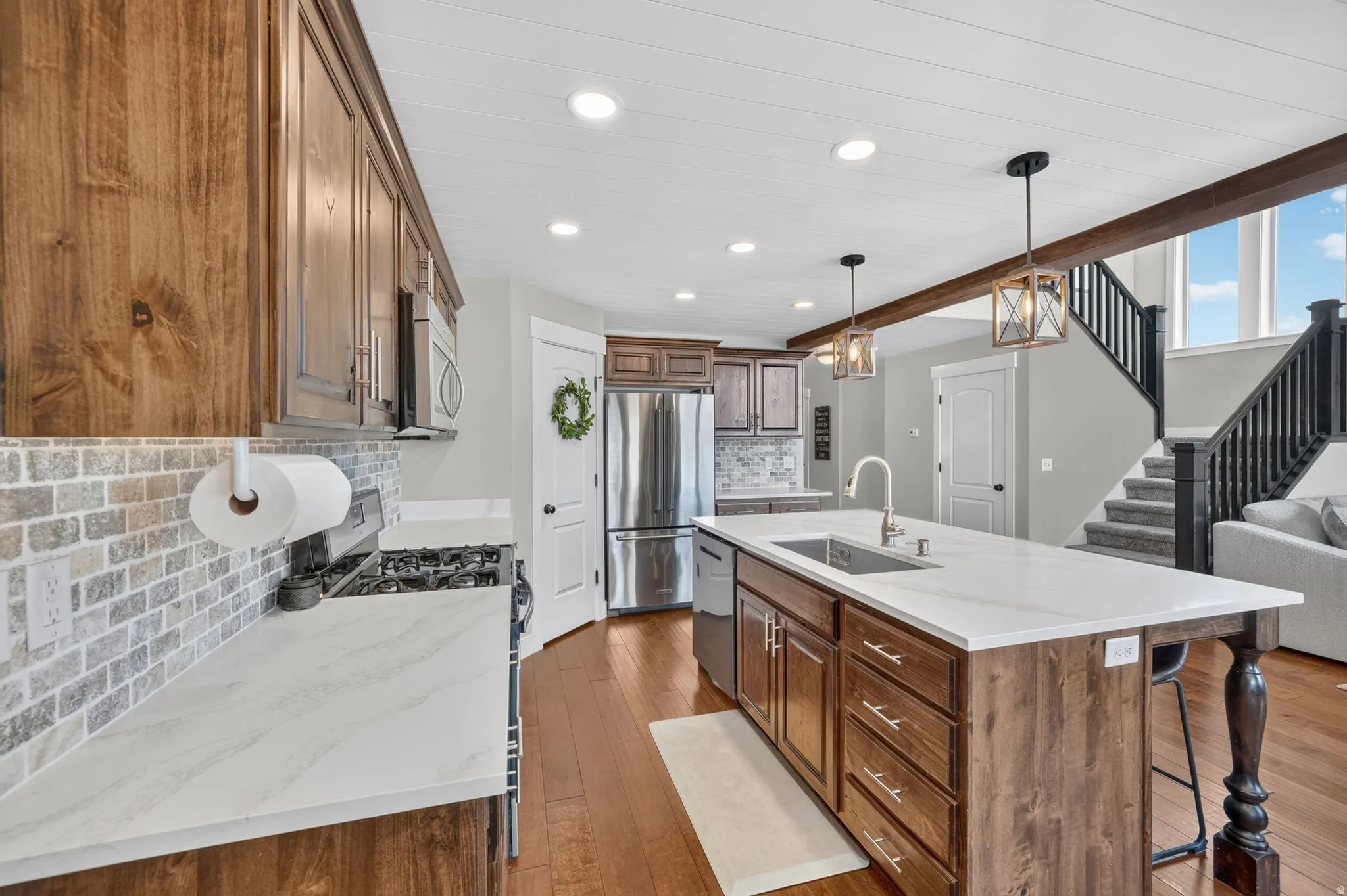 Hardwood flooring, wood-finish cabinetry, white countertops, brick-patterned backsplash, and a stainless steel refrigerator