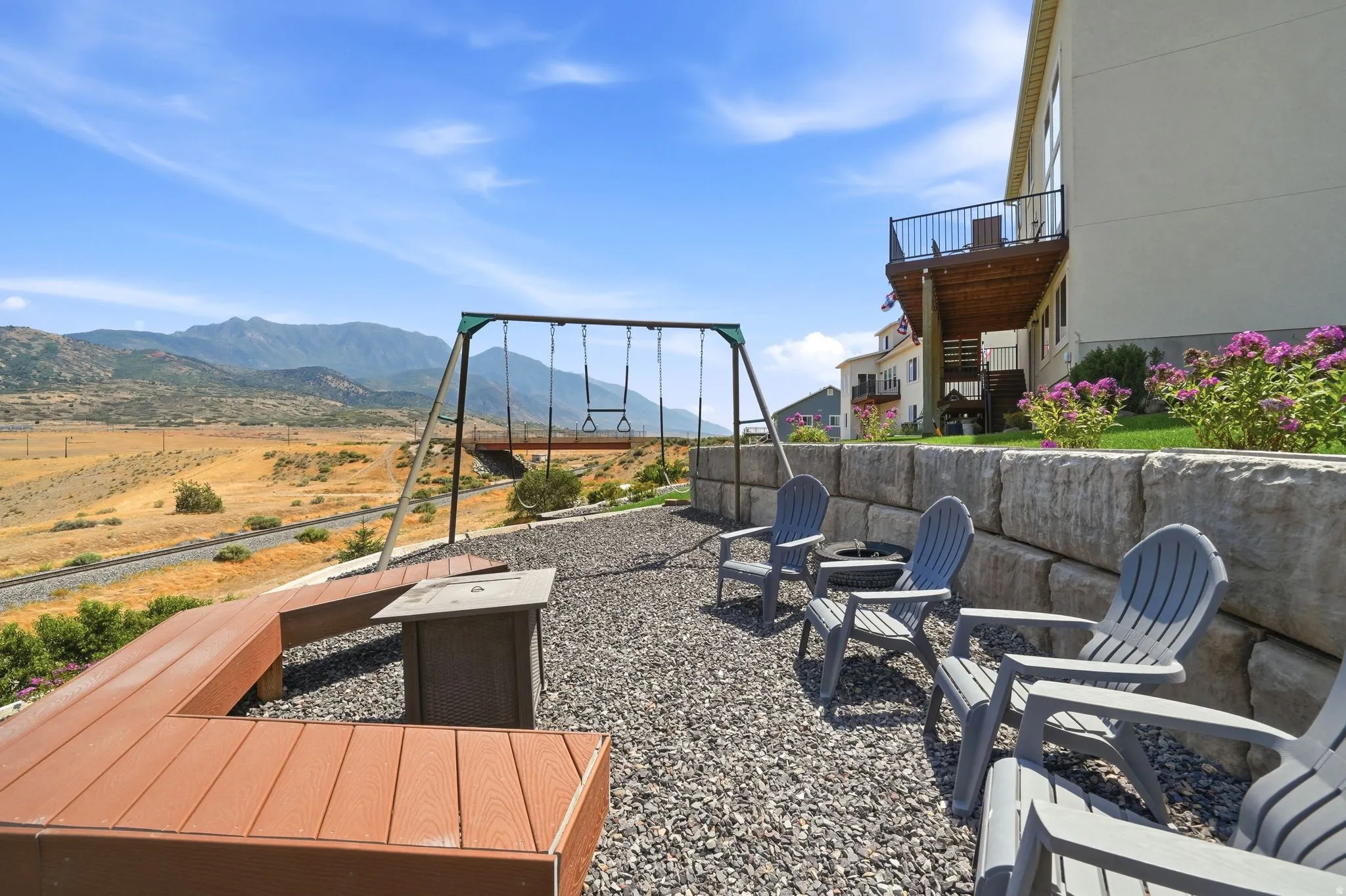 Gravel patio area featuring a built-in fire pit, composite L-shaped bench, a swing set, and a stacked stone retaining wall