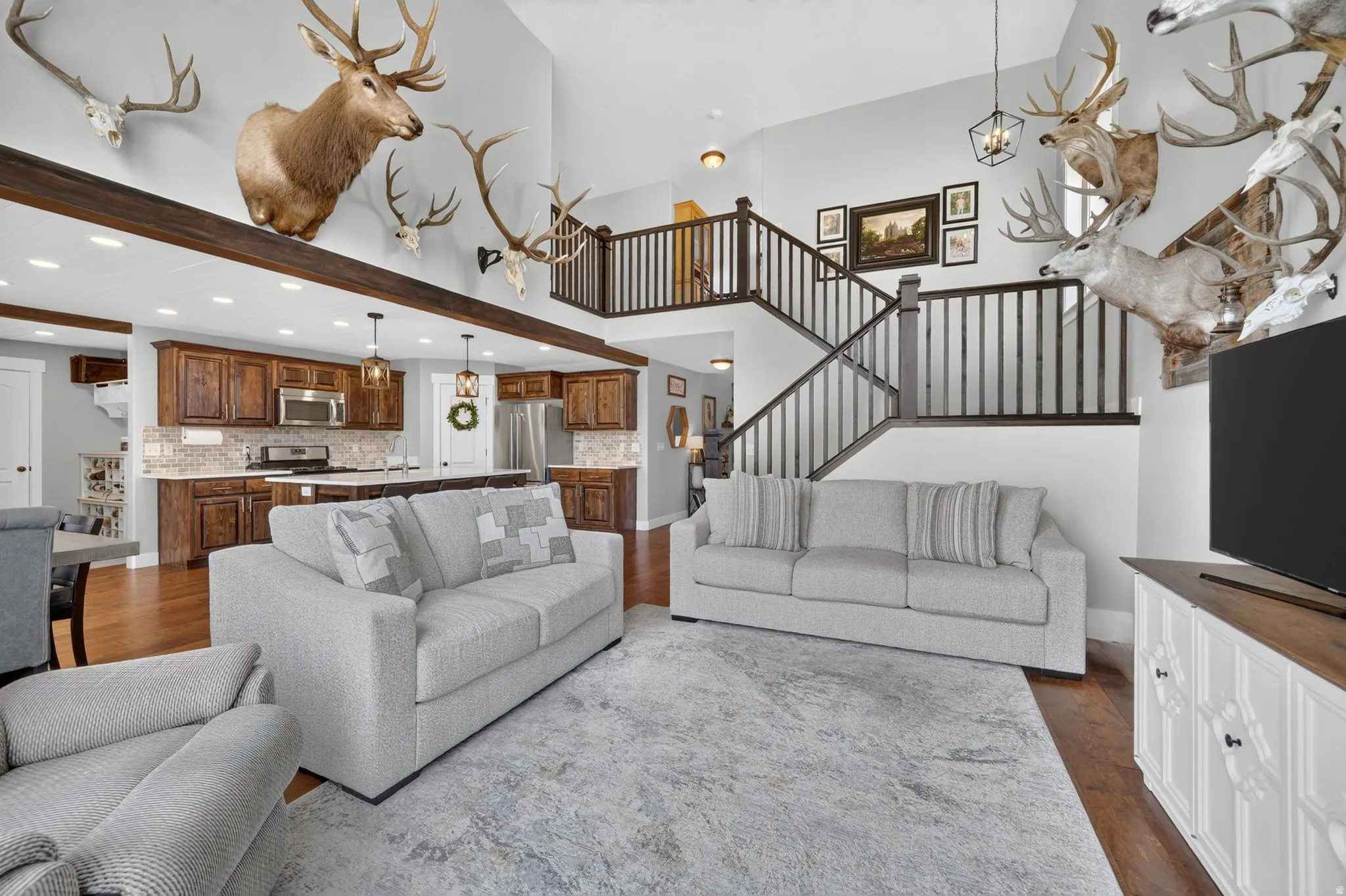 Open-concept living area featuring a vaulted ceiling with exposed wood beams, a two-story staircase with dark wood railings, and rich wood-finish flooring