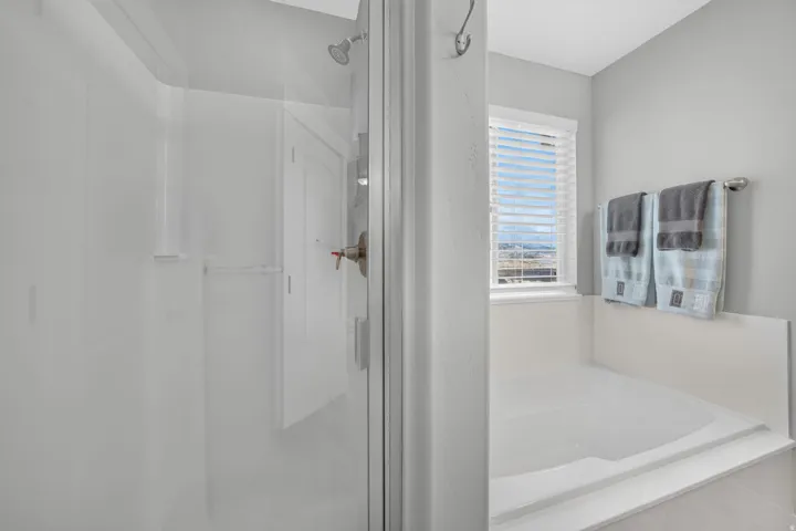 Glass-enclosed shower with brushed nickel fixtures, built-in soaking tub, and window with horizontal blinds