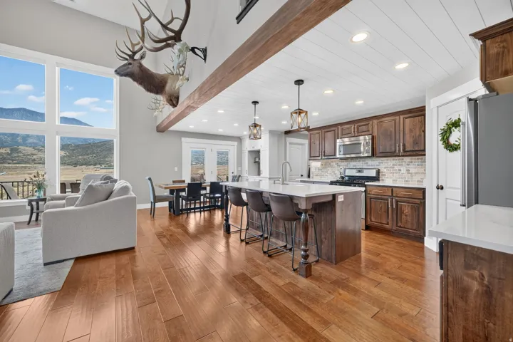 High ceilings with exposed wood beams, expansive floor-to-ceiling windows, wood-finish flooring, a kitchen island with seating, and stainless steel appliances