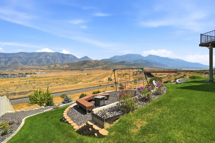 Expansive backyard featuring a manicured lawn, tiered landscaping with stone retaining walls, and a built-in fire pit with bench seating
