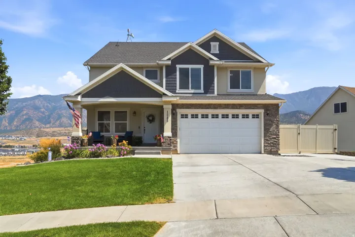 Two-story residence featuring a two-car garage, stone and siding exterior, front porch, and a landscaped front yard with a concrete driveway