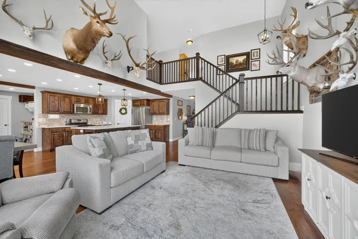 Open-concept living area featuring a vaulted ceiling with exposed wood beams, a two-story staircase with dark wood railings, and rich wood-finish flooring