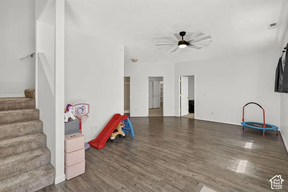 Wood-finish flooring, recessed lighting, ceiling fan with integrated lighting, white interior walls, and carpeted stairs with a white handrail