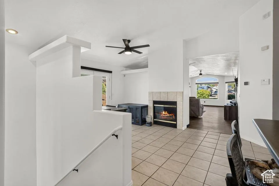Tiled flooring, ceiling fan, fireplace with a tile surround, built-in recessed lighting, and a partial staircase with railing