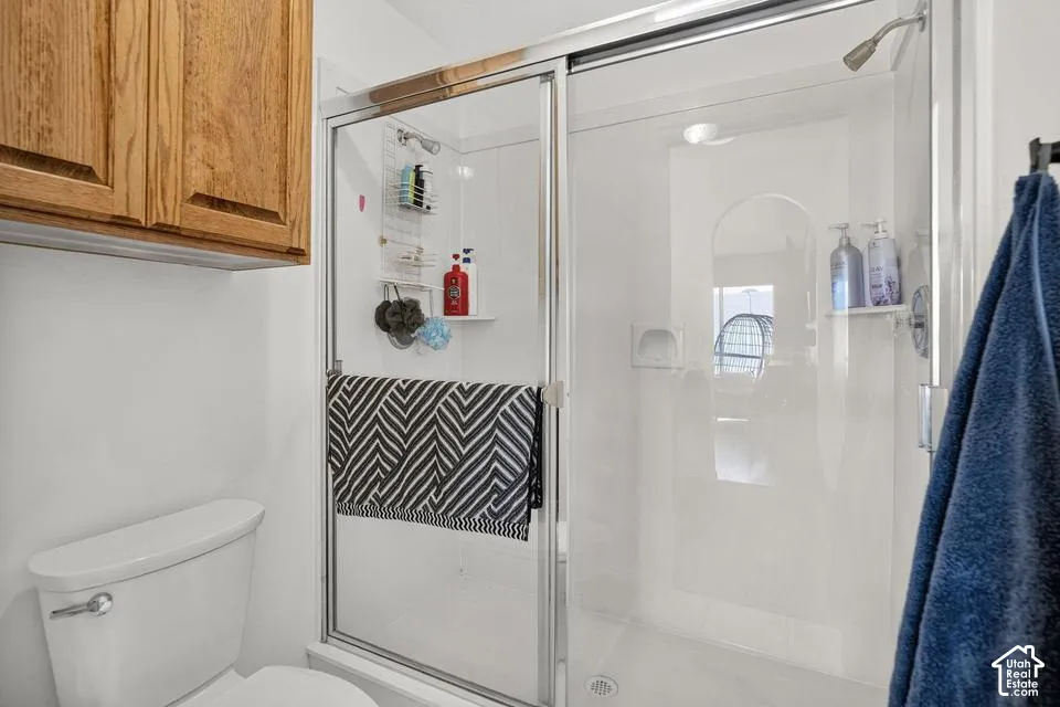 White shower stall with clear glass sliding door, integrated shelving, and a chrome showerhead
