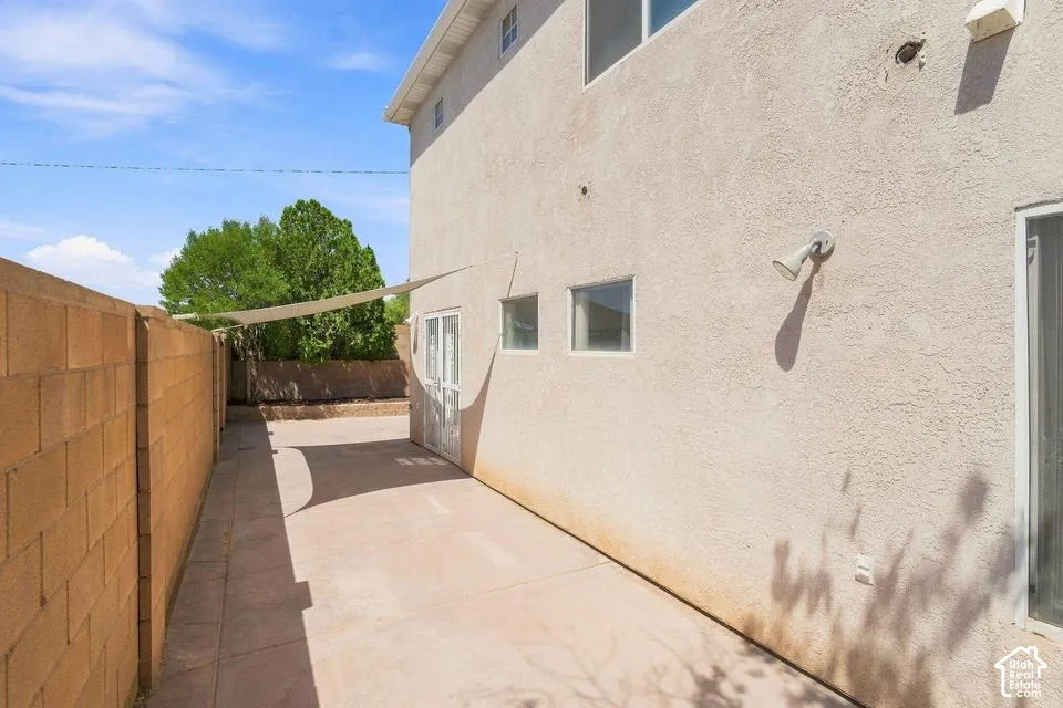 Stucco exterior with multiple windows, concrete patio, and block privacy wall