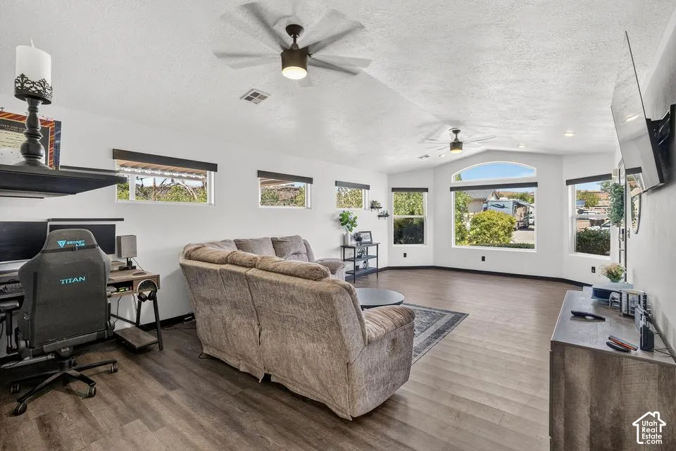 Expansive living area with wood-finish flooring, vaulted ceilings, and multiple windows