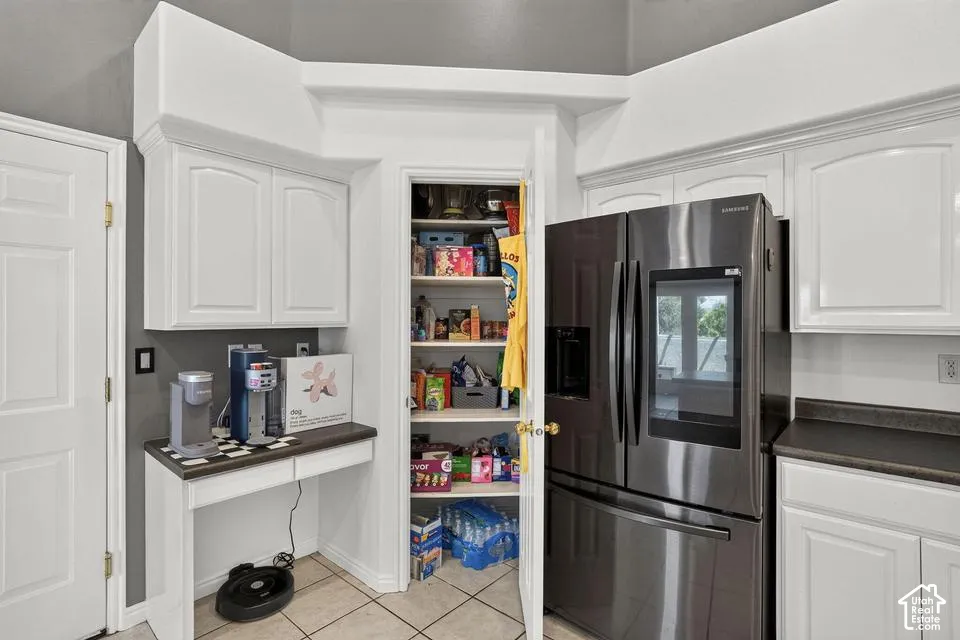 White cabinetry with crown molding, stainless steel refrigerator, built-in pantry shelving, tile flooring, and a dedicated beverage station