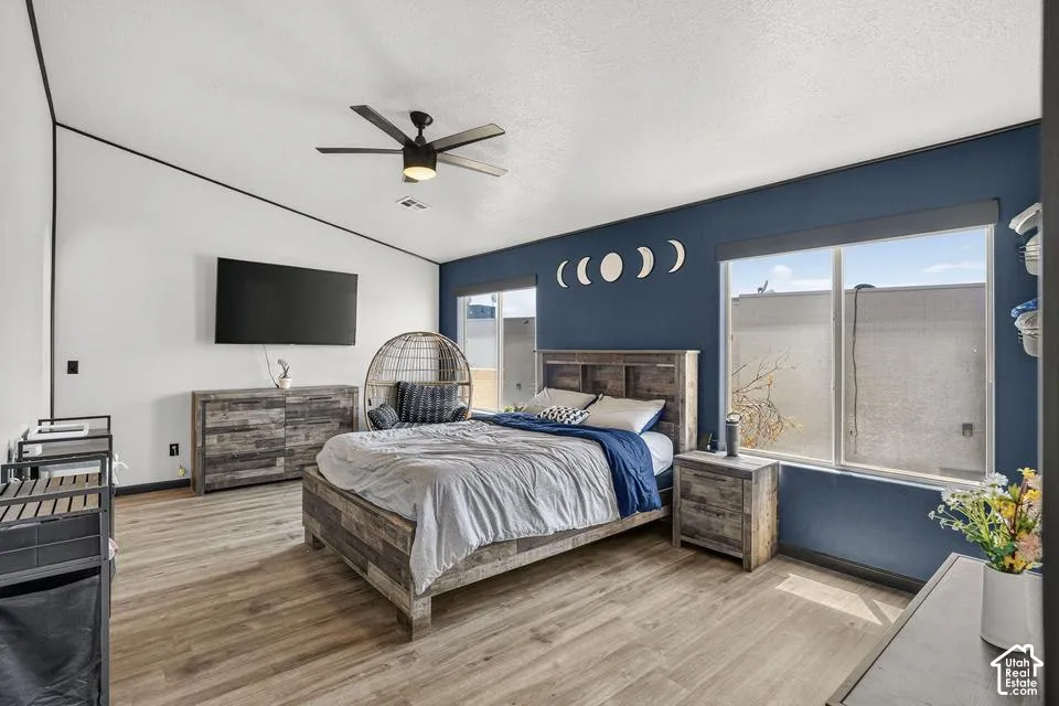 Sloped ceiling, wood-finish flooring, two large windows, ceiling fan, and accent wall