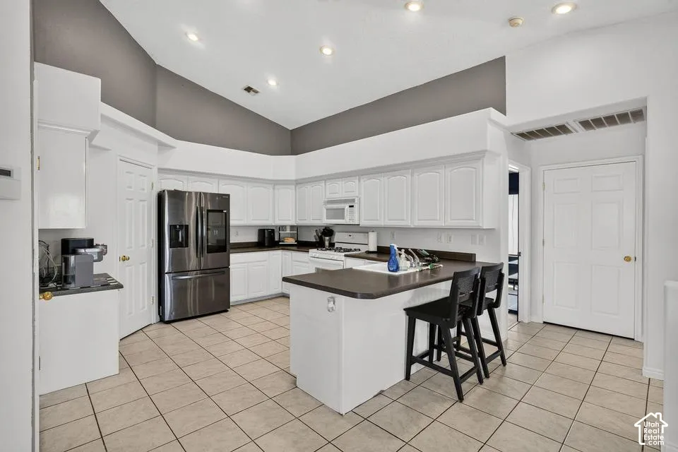 Kitchen featuring white cabinetry, dark countertops, stainless steel refrigerator, tile flooring, and recessed lighting