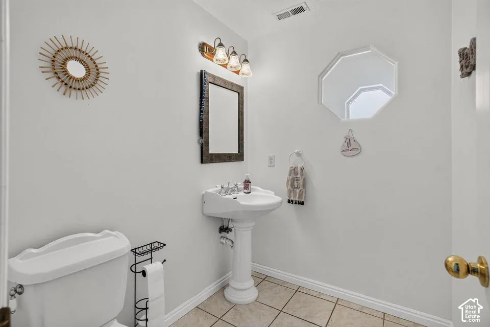 White pedestal sink with a dual-handle faucet, wall-mounted vanity light, and a framed rectangular mirror