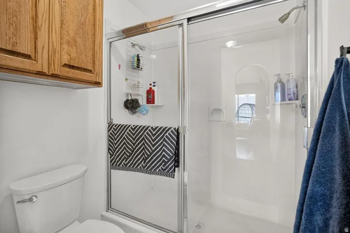 White shower stall with clear glass sliding door, integrated shelving, and a chrome showerhead