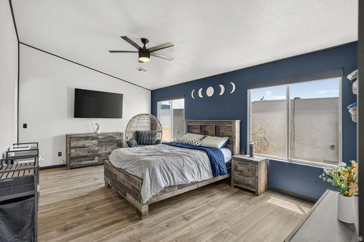 Sloped ceiling, wood-finish flooring, two large windows, ceiling fan, and accent wall