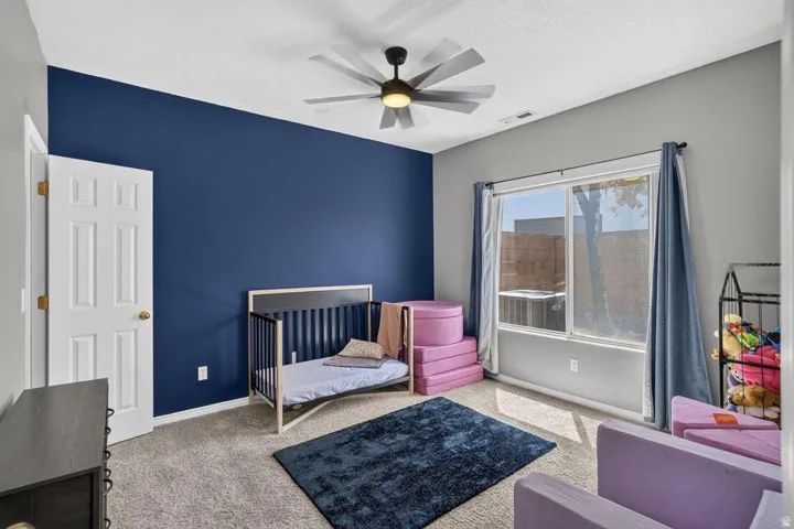 Carpeted flooring, a ceiling fan, and a large window providing natural light