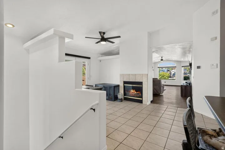 Tiled flooring, ceiling fan, fireplace with a tile surround, built-in recessed lighting, and a partial staircase with railing