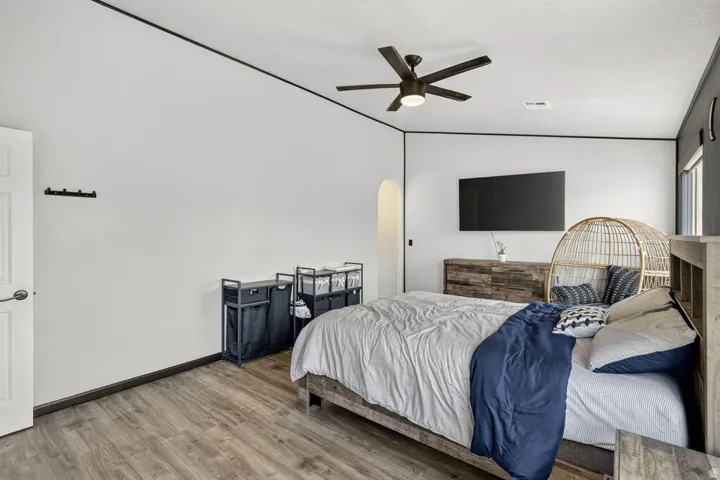 Wood-finish flooring, ceiling fan with integrated lighting, wall-mounted television, and an arched entry
