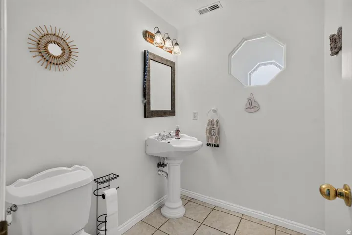 White pedestal sink with a dual-handle faucet, wall-mounted vanity light, and a framed rectangular mirror