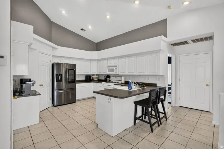 Kitchen featuring white cabinetry, dark countertops, stainless steel refrigerator, tile flooring, and recessed lighting