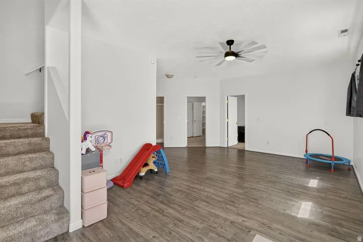 Wood-finish flooring, recessed lighting, ceiling fan with integrated lighting, white interior walls, and carpeted stairs with a white handrail