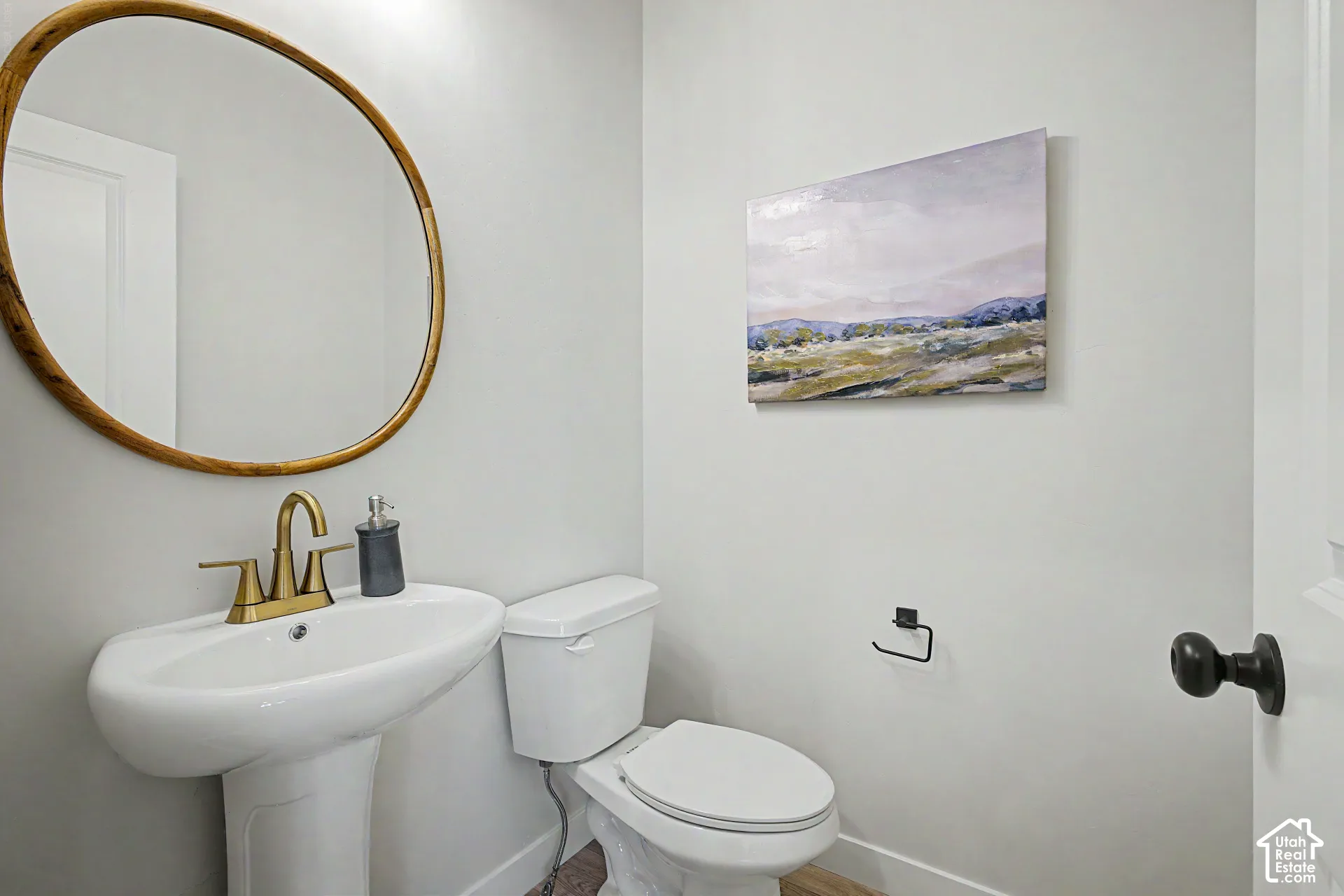 Pedestal sink with brass-finish faucet, circular mirror with wood-finish frame, and a white toilet