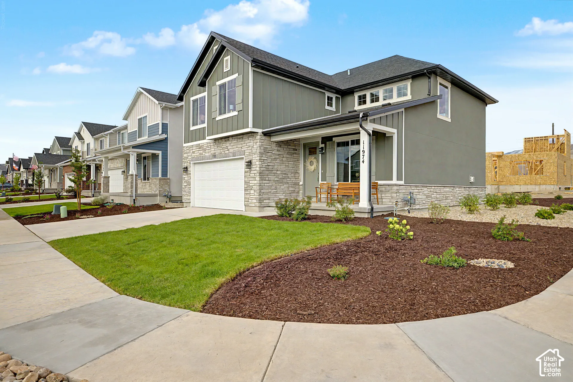 Contemporary exterior featuring a stone and siding facade, an attached garage, a covered front porch, and manicured landscaping