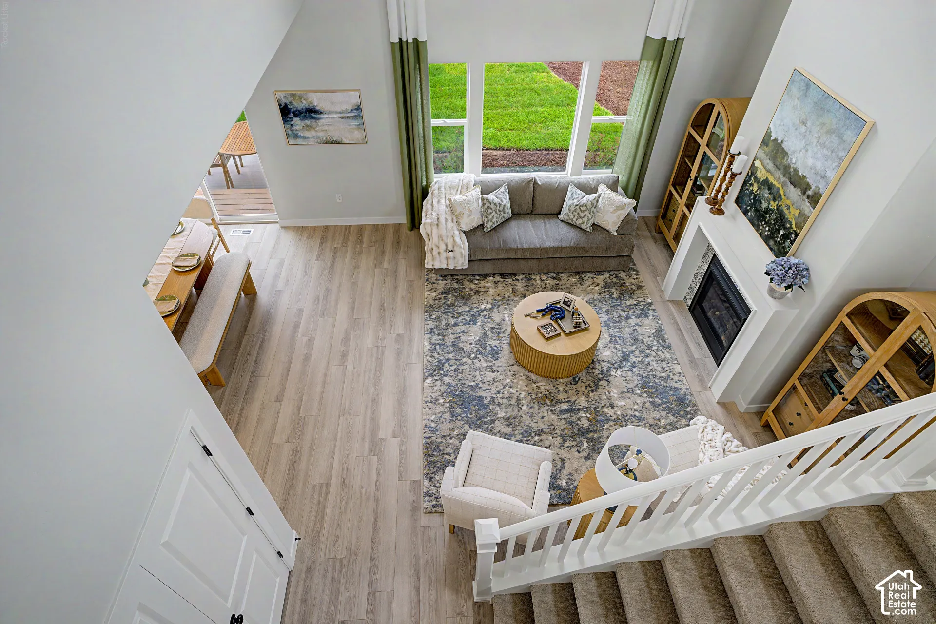Spacious room featuring wood-finish flooring, a contemporary fireplace, large windows, and a carpeted staircase with a white railing system