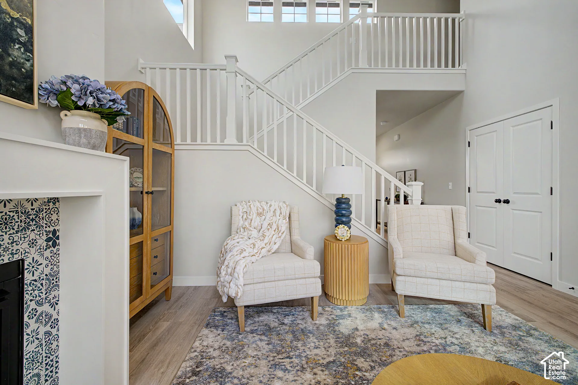 Two-story staircase with white railings, light wood-finish flooring, patterned fireplace surround, and recessed lighting