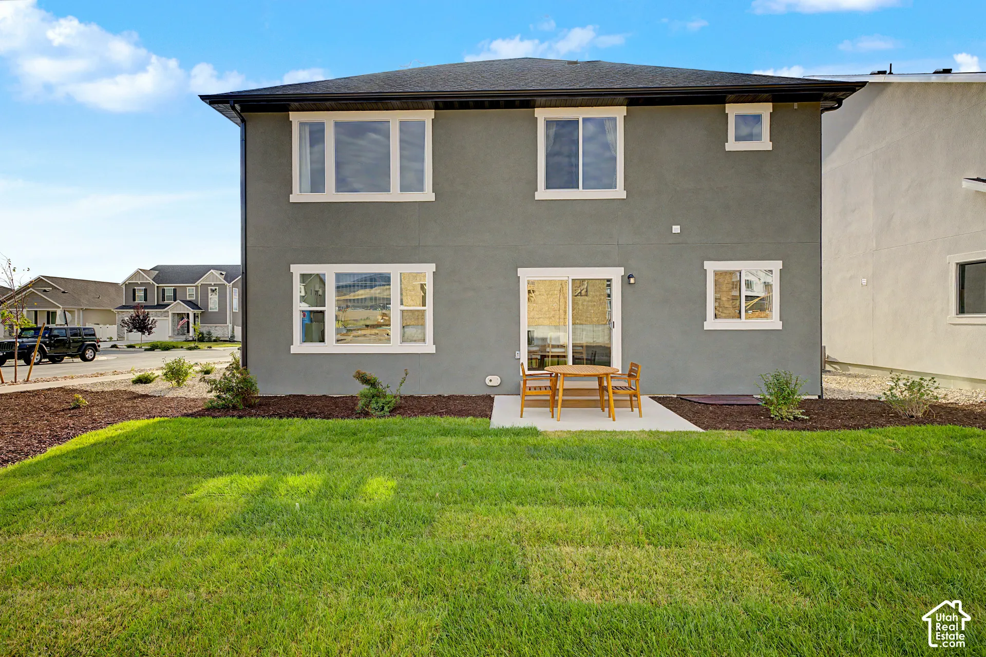 Expansive lawn area with a concrete patio, sliding glass door, and multiple windows