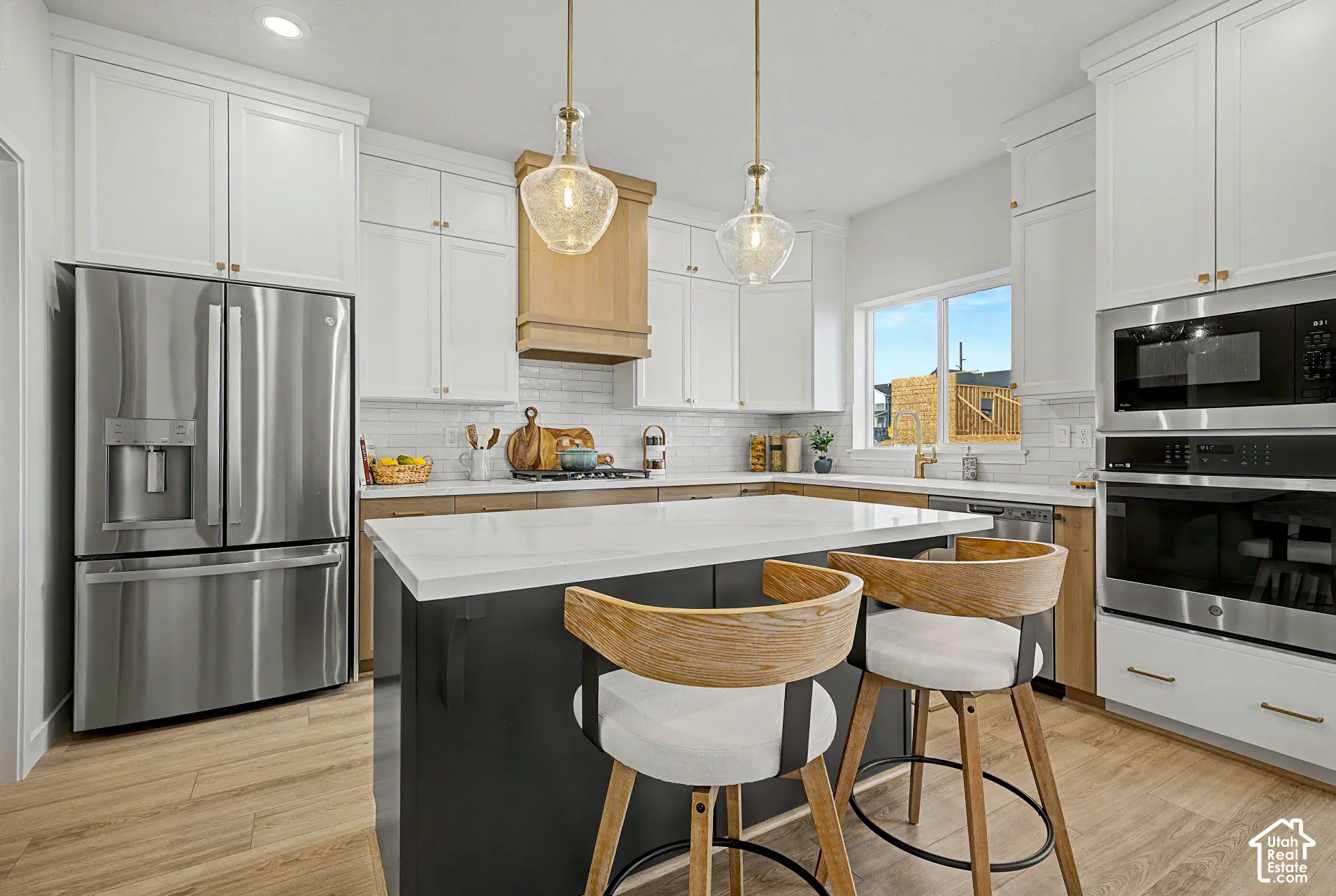 Gourmet kitchen featuring white shaker cabinetry, stainless steel appliances, a center island with a white countertop, wood-finish flooring, and pendant lighting
