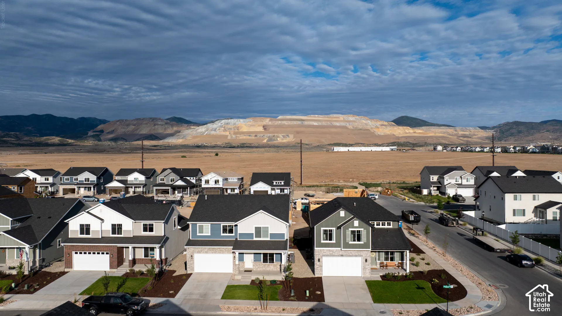 Residential development with multiple two-story homes featuring attached garages, landscaped front yards, and a backdrop of expansive open land with distant mountains