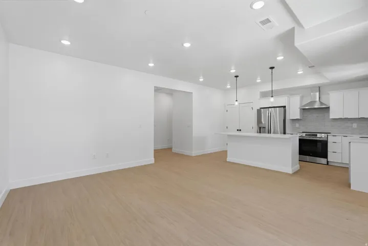 Open-concept living space featuring wood-finish flooring, recessed lighting, and a kitchen with stainless steel appliances, white cabinetry, and a central island