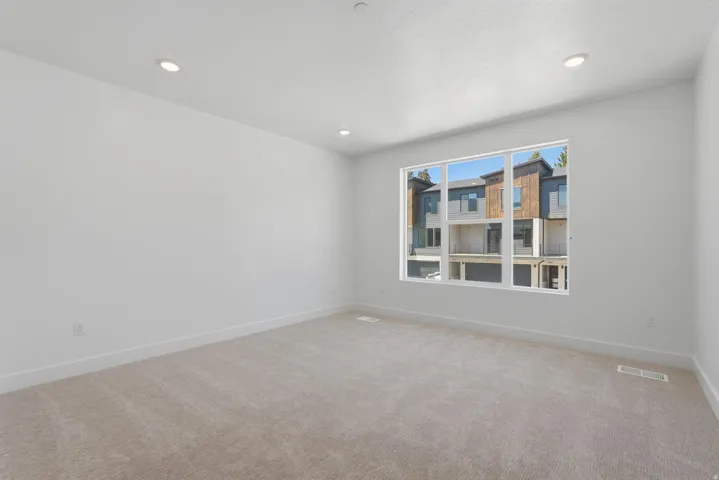 Recessed lighting, large window, neutral carpeting, and crisp white walls