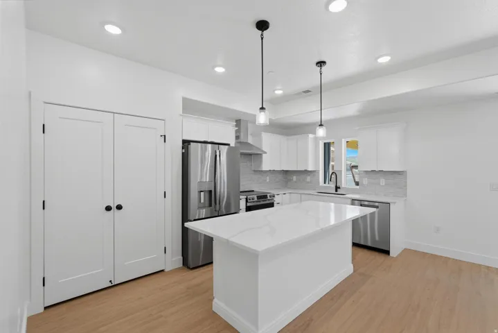 Modern kitchen featuring a central island with a light-toned countertop, stainless steel appliances, white cabinetry, and recessed lighting