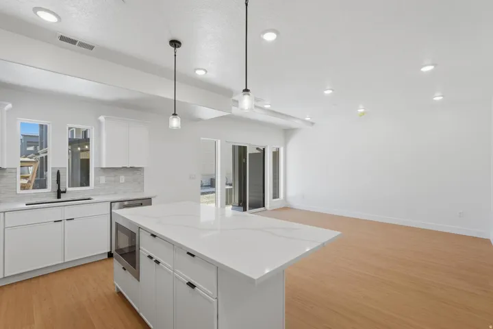 Modern kitchen featuring a large island with a quartz countertop, white cabinetry with black hardware, stainless steel dishwasher, and an integrated microwave