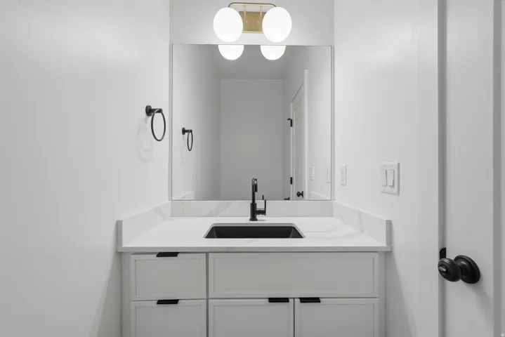White vanity with pull-out drawers, black hardware, an undermount sink, and a white countertop