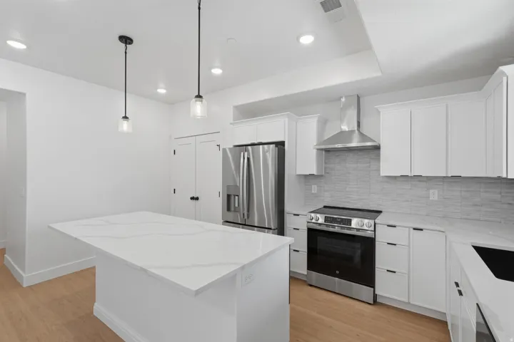 White cabinetry with contrasting black hardware, stainless steel appliances, light wood-finish flooring, white countertops, and a full-height tile backsplash