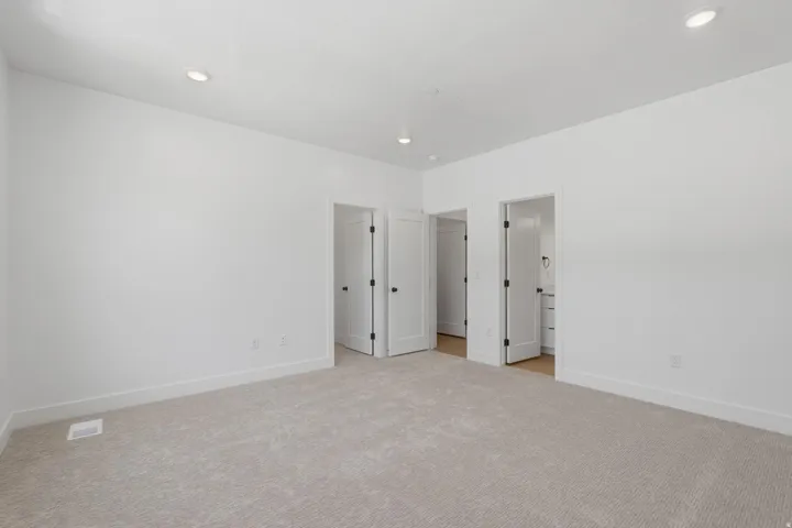 Neutral-toned carpeting, recessed ceiling lighting, and multiple paneled doors with dark hardware