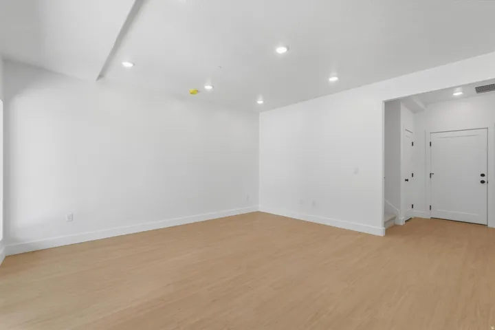 Recessed lighting, wood-finish flooring, white walls, and a white entry door with matte black hardware
