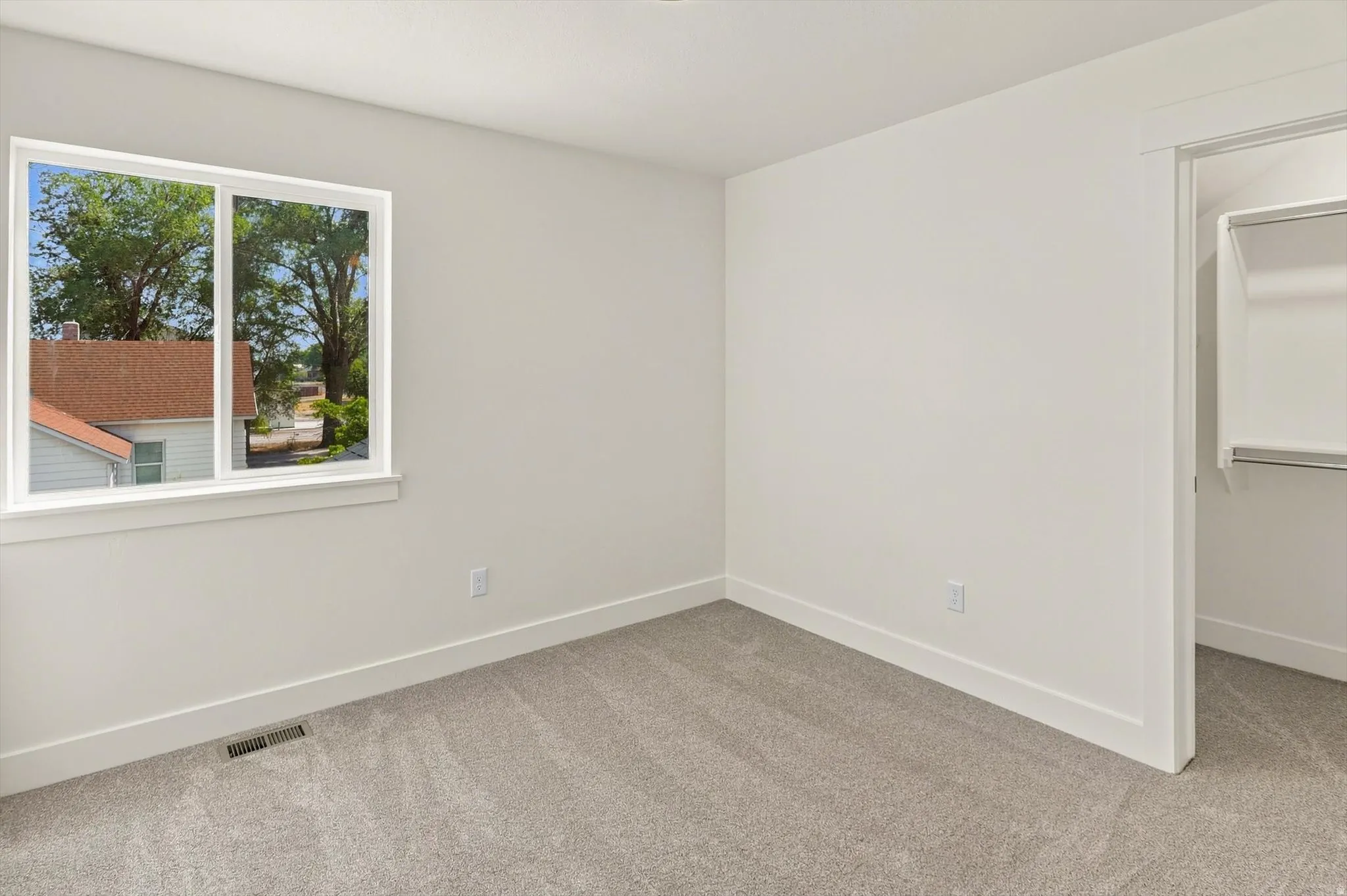 Carpeted interior space featuring a window with white trim, a built-in closet with shelving and hanging rod, and light-colored walls