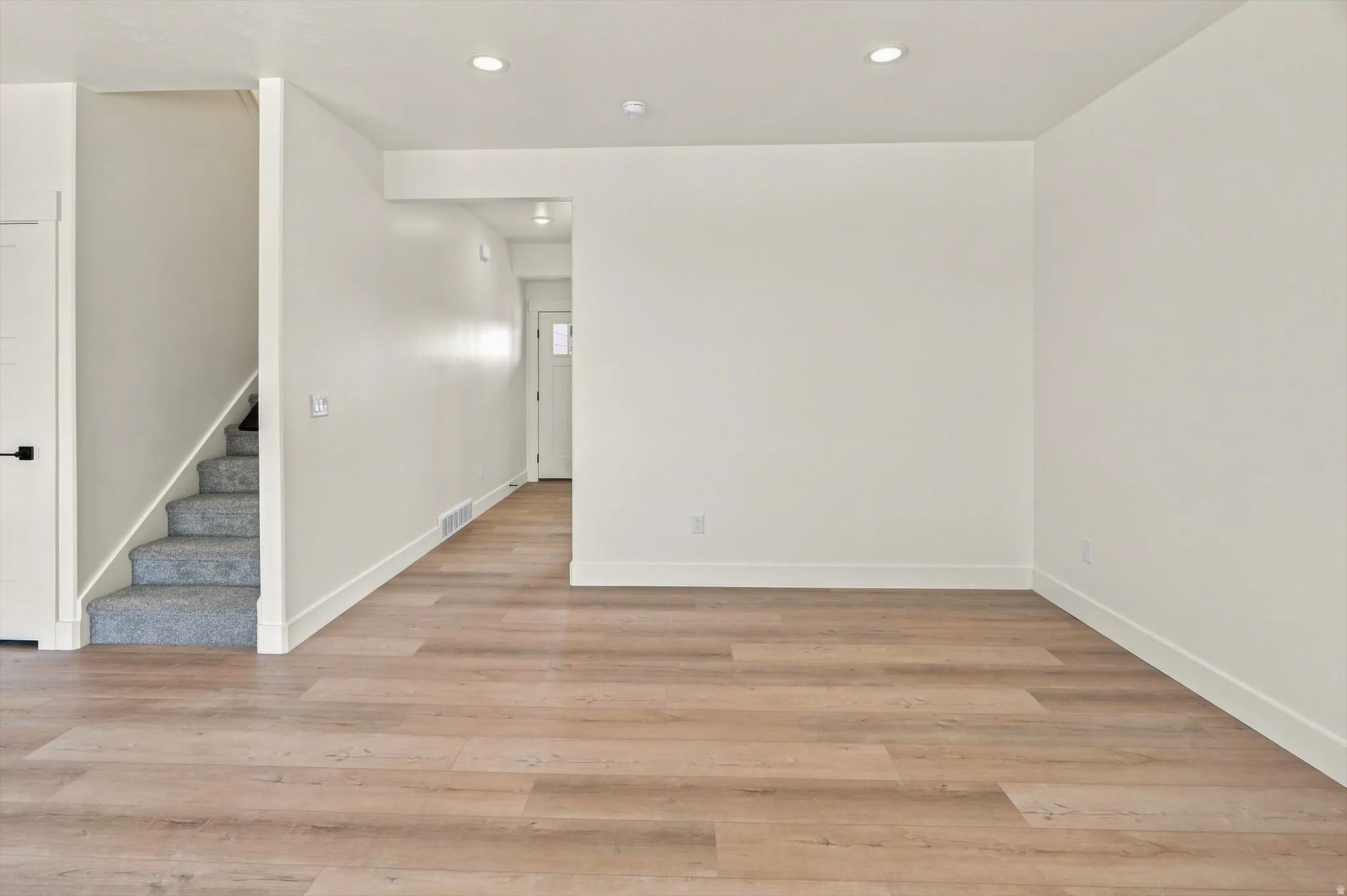 Open-concept living space with wood-finish flooring, recessed lighting, and crisp white walls