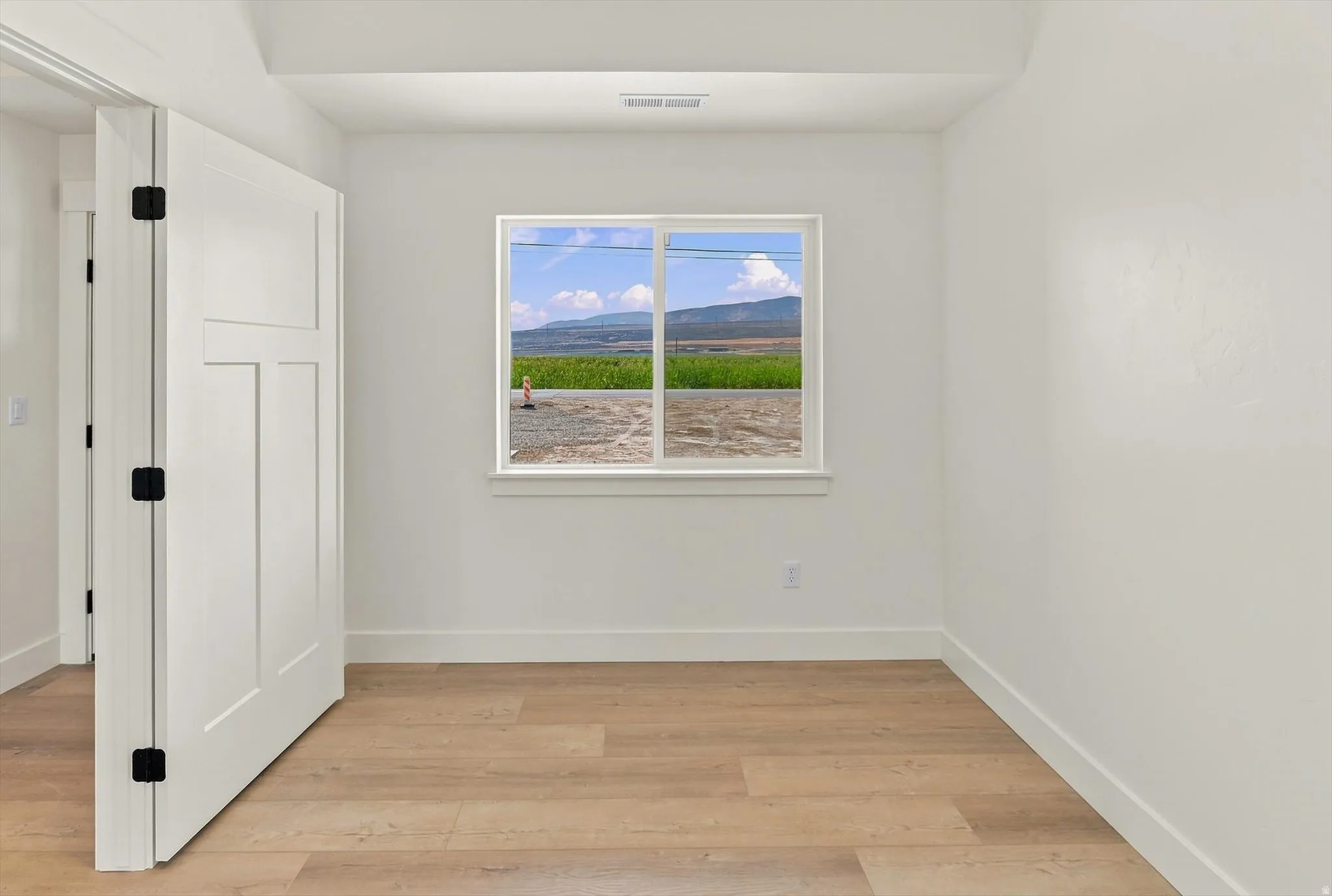 White interior walls, wood-finish flooring, white window trim, white paneled door with black hardware, and an exterior landscape with mountains and fields